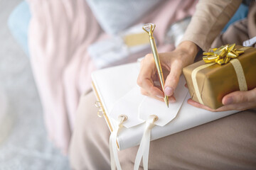 Obraz na płótnie Canvas Closeup female hands writing Christmas festive congratulations on card for gift box package