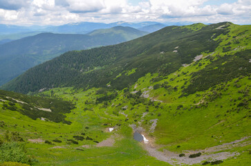 Fototapeta premium Panoramic aerial view of small mountain lake in the valley between the green slopes of the mountains. Carpathians, Ukraine