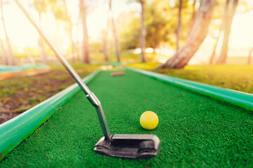Yellow ball with stick for sports mini golf on green grass background with sunlight - obrazy, fototapety, plakaty