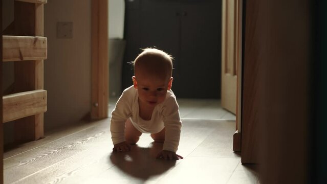 happy baby boy crawling on floor toddler exploring home curious infant having fun enjoying childhood. Little Cute smilling Child in white bodysuit try to stand up walk first steps barefoot on floor