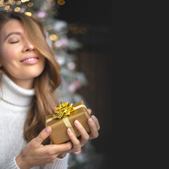 Closeup smiling young blonde woman holding luxury golden Christmas gift box celebrating holiday