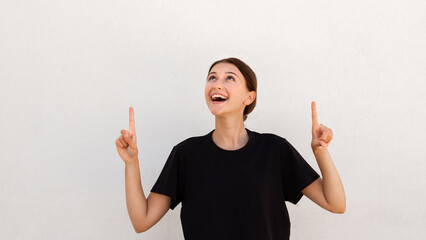 Portrait of excited young woman pointing upwards over white background. Caucasian woman wearing...