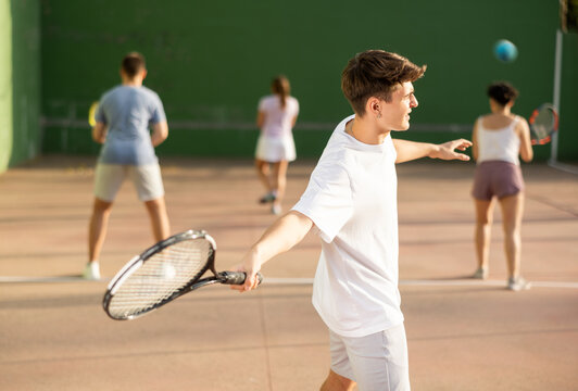 Concentrated young Latin American frontenis player swinging string racquet to hit ball on outdoor walled court on sunny summer day. Sport and active lifestyle concept