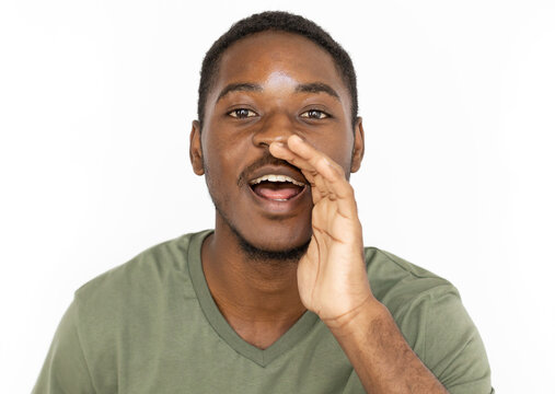 Whispering young man holding hand near mouth. Male African American model in green T-shirt holding hand near his mouth sharing secret or gossiping. Secrecy, privacy concept.