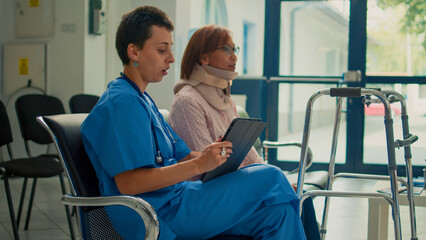 Nurse consulting patient with neck collar brace and walking frame, taking notes about accident injury on tablet. Doing checkup visit with woman wearing cervical foam and impairment.