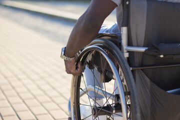 Close-up of muscular male arm rolling wheelchair wheel in habitual manner. Middle-aged man with physical disability spending time outdoors alone. Disability, healthcare, lifestyle concept.