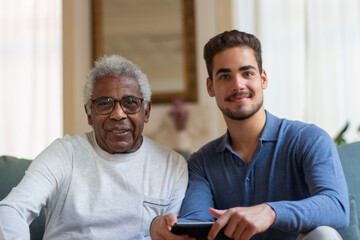 Portrait of happy grandfather and grandson having day together. Young man and old Latin man sitting...