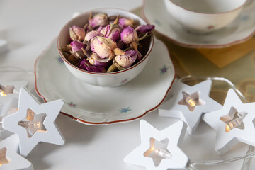 dried rose flower buds in a white porcelain tea cup and saucer and a star-shaped garland on the table
