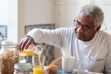 Portrait of senior man having breakfast in kitchen. Grey-haired man in glasses calmly sitting at...