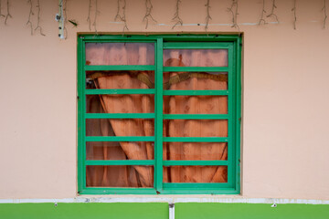 Green Window with a Orange Curtain Inside and Light Orange Background, Characteristic of the Town