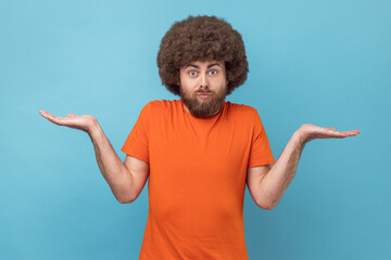 Clueless confused man with Afro hairstyle in T-shirt shrugging shoulders as doesn't know answer,...