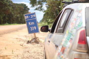 Carro de passeio em frente a placa indicativa de quilometragem na BR-319, no Amazonas 