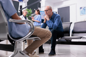 Stressed exhausted senior man patient sitting on chair in hospital reception waiting for physician...
