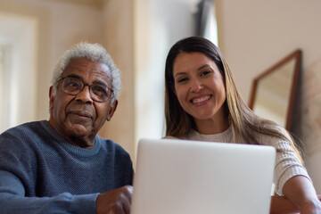 Portrait of happy woman and aged man using computer.Grey-haired man and his granddaughter spending time together sitting indoors searching information in internet.Taking care of elderly people concept