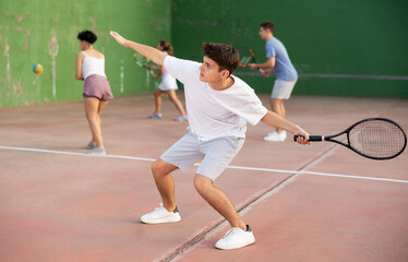 Young male sportsman preparing to hit ball with racket. Frontenis game on outdoor court
