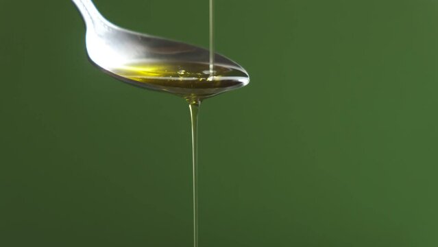 Aceite de oliva cayendo en la cuchara en fondo verde