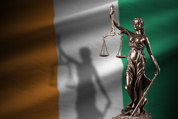 Ivory Coast flag with statue of lady justice and judicial scales in dark room. Concept of judgement...