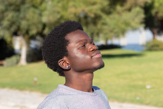 Portrait of young Black man enjoying warm sunny day in park. Happy short-haired African American guy with stylish earring smiling and having good time outside. Lifestyle, youth, leisure time concept.