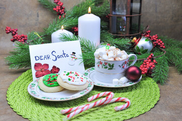 Christmas table setting with Santa greeting card hot chocolate with marshmallow toppings and cookies candy cane setting