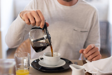 Man sitting at kitchen table and pouring coffee into cup. Medium shot of unrecognizable man having yummy breakfast at home, enjoying food, getting ready for new day. Morning routine, food concept