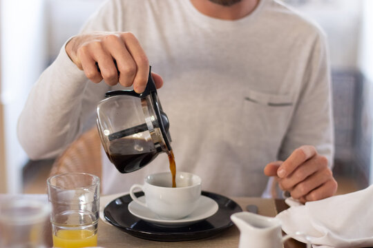 Man sitting at kitchen table and pouring coffee into cup. Medium shot of unrecognizable man having yummy breakfast at home, enjoying food, getting ready for new day. Morning routine, food concept