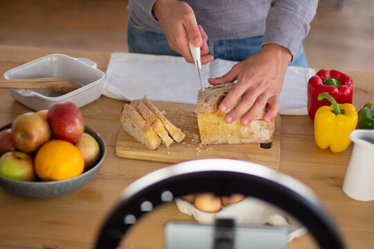 Close-up of male food bloggers hands cutting bread on camera. Cheerful man creating tutorial video for healthy culinary blog talking about recipes of home meal. Creating of food blogs, cooking concept