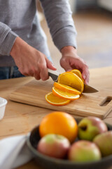Close-up of male hands slicing big juicy orange. Unrecognizable man standing in kitchen holding orange on cutting board and preparing healthy salad for dinner. Cooking, healthy food at home concept