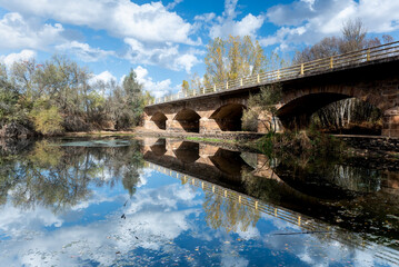 bridge reflected in the water next to sky with clouds