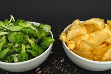 Two white bowls - one with green lettuce leaves, the second with chips, on a black background. Healthy food, health care, healthy lifestyle