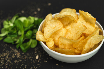 Two white bowls - one with green lettuce leaves, the second with chips, on a black background. Healthy food, health care, healthy lifestyle
