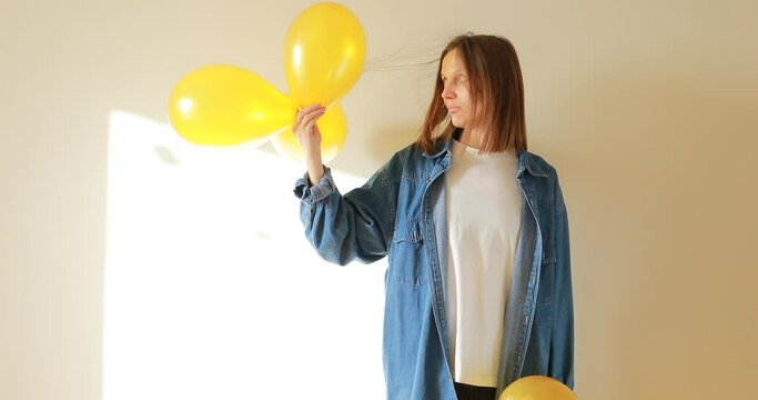 Young beautiful woman having fun with yellow air balloon indoors. Surprised girl is rubbing a balloon against her hair and electricity is generated. Laws of physics.