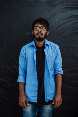Obraz premium Indian smiling young student in blue shirt and glasses posing on school blackboard background