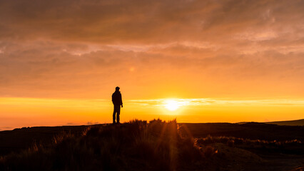 A man standing on a mountain as the sun sets. Panoramic photo, sunset silhouette