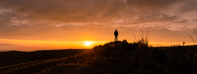 A man standing on a mountain as the sun sets. Panoramic photo, sunset silhouette
