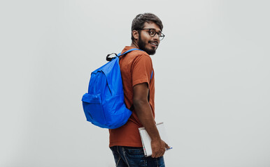  Indian student with blue backpack, glasses and notebook posing on gray background. The concept of education and schooling. Time to go back to school