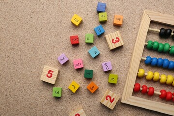 Wooden cubes with numbers and multiplications near abacus on fiberboard, flat lay. Space for text