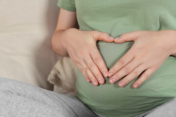 Pregnant woman making heart with her hands on sofa, closeup