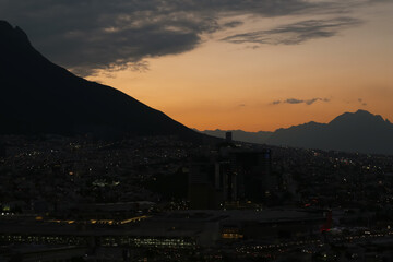 Picturesque view of sunset with dark clouds above big mountains and evening city