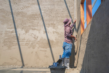 Plakat Side view of builder worker using long trowel to polishing cement wall inside of house construction site