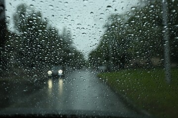 Blurred view of road through wet car window. Rainy weather - obrazy, fototapety, plakaty