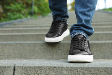 Man in stylish black sneakers walking down stairs, closeup