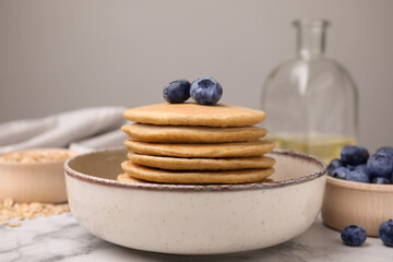Fototapeta na wymiar Tasty oatmeal pancakes with blueberries on white marble table, closeup