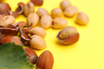 Obraz na płótnie Canvas Tasty organic hazelnuts and leaves on yellow background, closeup