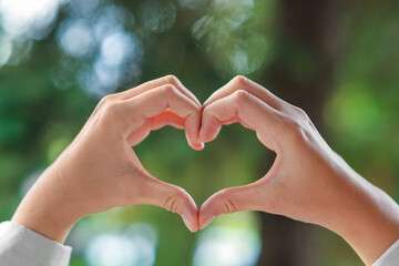Woman showing heart gesture with hands against blurred background, closeup. Love concept