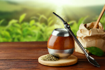 Calabash with mate tea and bombilla on wooden table outdoors. Space for text