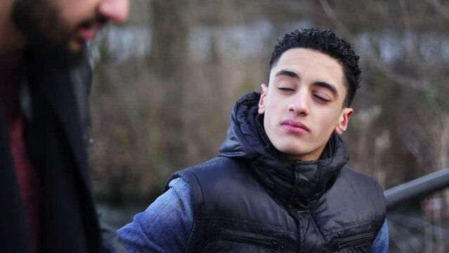 Overshoulder of a young middle eastern man sniffing and talking to his friend
