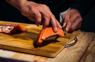 Close up of Chef cook hands chopping salmon fish for traditional Asian cuisine with Japanese knife. Professional Sushi chef cutting seafood japanese chefs are making salmon fish sashimi. dark tone