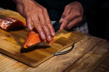 Close up of Chef cook hands chopping salmon fish for traditional Asian cuisine with Japanese knife. Professional Sushi chef cutting seafood japanese chefs are making salmon fish sashimi. dark tone