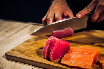 Close up of Chef cook hands chopping tuna fish for traditional Asian cuisine with Japanese knife. Professional Sushi chef cutting seafood japanese chefs are making tuna fish sashimi. dark tone