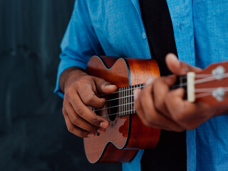 Fototapeta premium Indian young man in a blue shirt and glasses playing the guitar in front of the school blackboard